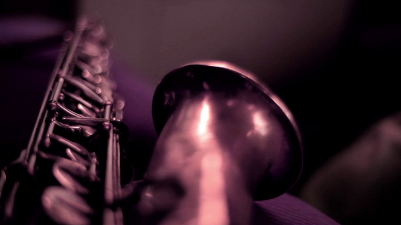 •0 Xpress2Brest_Film_Kate_Thompson_Gorry Close-up shot of a saxophone's bell and part of its key system, with a warm, dim lighting creating a soft, moody atmosphere. The focus is on the bell, with the keys slightly blurred in the background. The image conveys a sense of intimacy with the instrument.