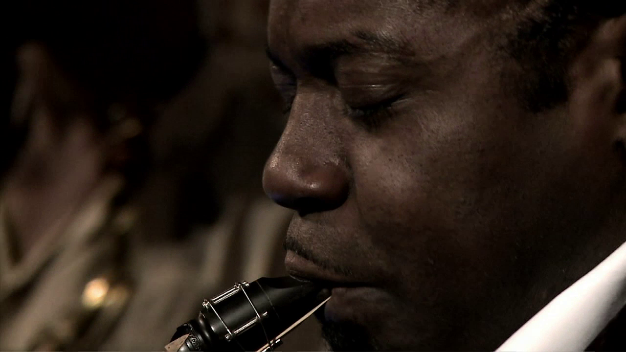 •13 Xpress2Brest_Film_Kate_Thompson_Gorry Close-up of a man with closed eyes playing a saxophone. The intimate and emotional moment captures the musician's focus and connection with the instrument. The background is blurred, keeping the attention on the man's expressive face and the saxophone mouthpiece.