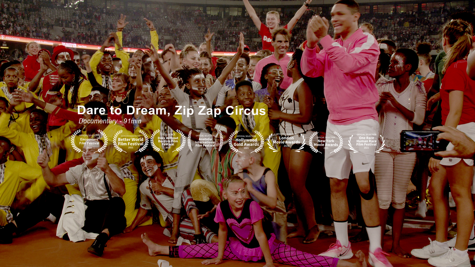 A vibrant, joyful crowd of diverse individuals, including performers in colorful costumes, celebrate together in an outdoor setting. An overlay of text reads "Dare to Dream, Zip Zap Circus" with multiple film festival laurels displayed beneath.