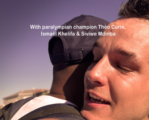Poster for "The Madiba Challenge" shows two men embracing warmly. Text reads, "30 km swim round Robbin Island, 100 km cycle ride through Cape Town. With paralympian champion Théo Curin, Ismaël Khelifa & Siviwe Mdimba. Broadcast on France Télévisions for the Paralympics, Paris 2024.