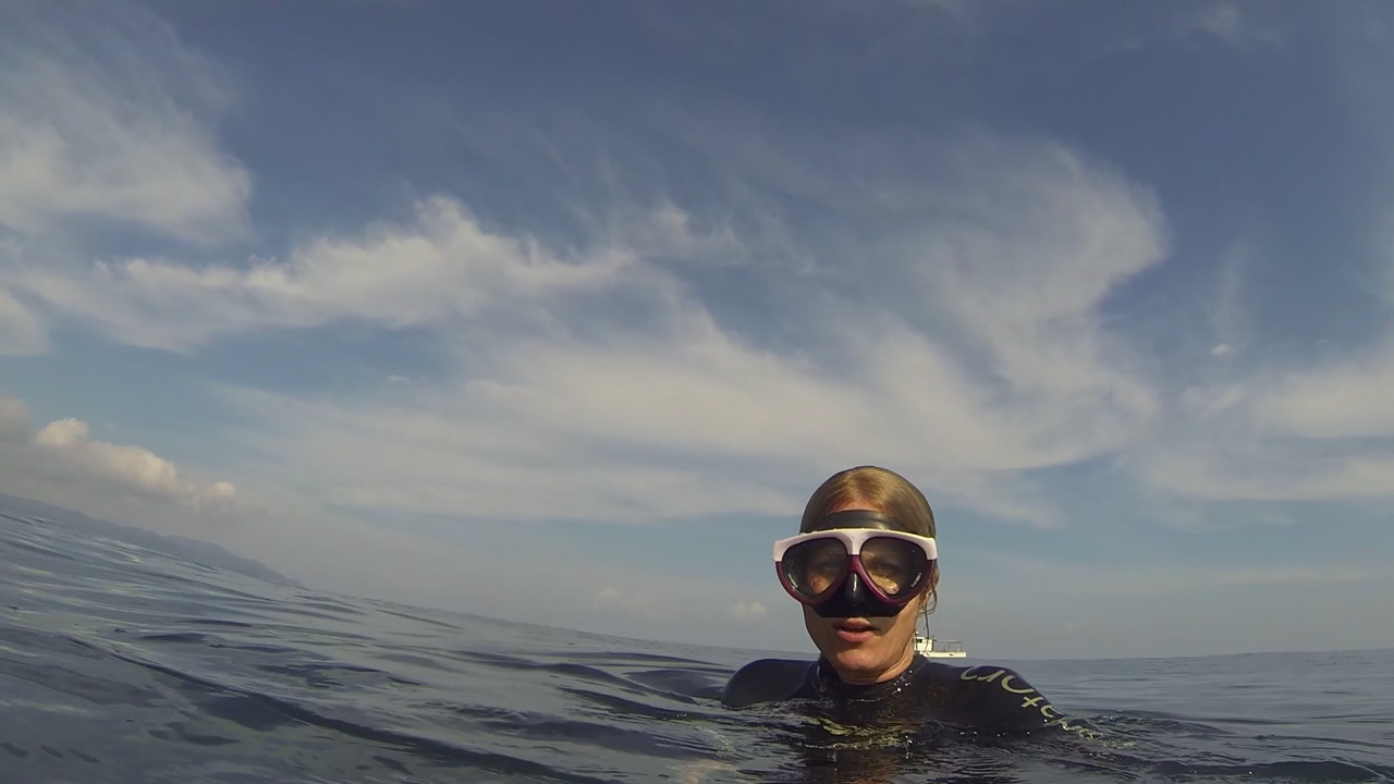 A person wearing snorkeling gear, including a mask and snorkel, is in the ocean with their head just above the water. The sky above is clear with wispy clouds and the horizon is visible in the distance.