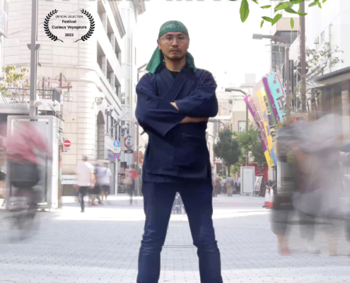 Film poster for "Japan, The Fight of a Tea Master" featuring the tea master standing confidently on a busy street, with a blurred crowd around him. He wears a headband, apron, and cross-armed pose amidst building facades and a clear sky in the background. Text includes film credits.